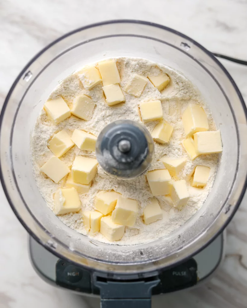 cubes of butter sit in flour in a food processor