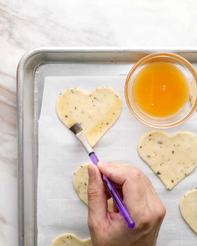 a hand brushes on egg wash on a heart shaped pie crust