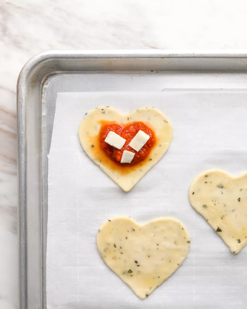 cubes of mozzarella cheese are placed on top of pizza sauce and pepperoni on heart shaped pie crust