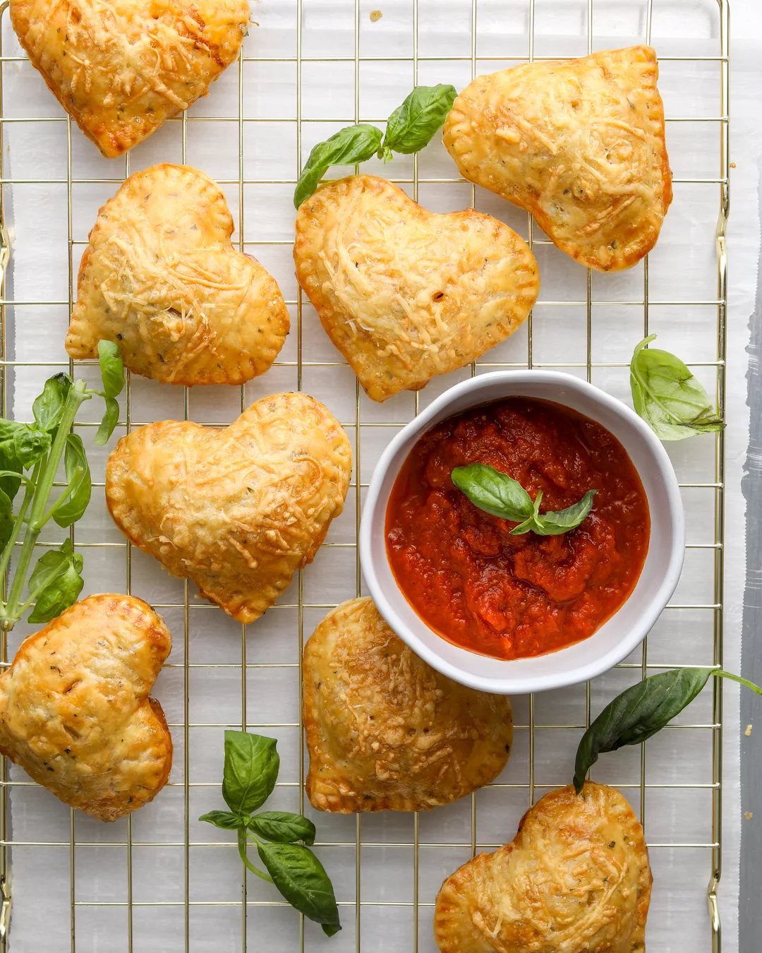 small pizza hand pies hot pockets sit on a wire cooling rack with pizza dipping sauce and basil