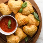 small pizza hand pies hot pockets sit on a wooden serving tray with pizza dipping sauce and basil