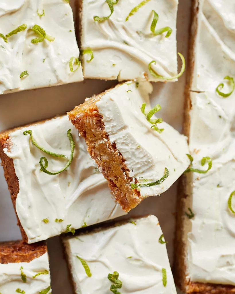 A coconut bar sits on its side showing the cross section of cookie base and lime cream cheese frosting