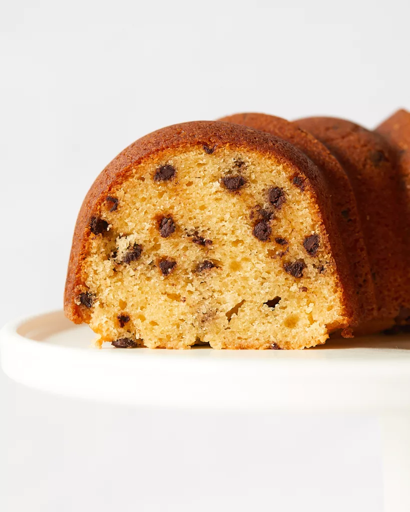 the cross-section of a slice of sour cream chocolate chip bundt cake on top of a white cake stand