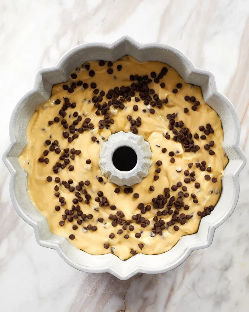 yellow cake batter in a traditional bundt cake tin. with mini chocolate chips sprinkled on top