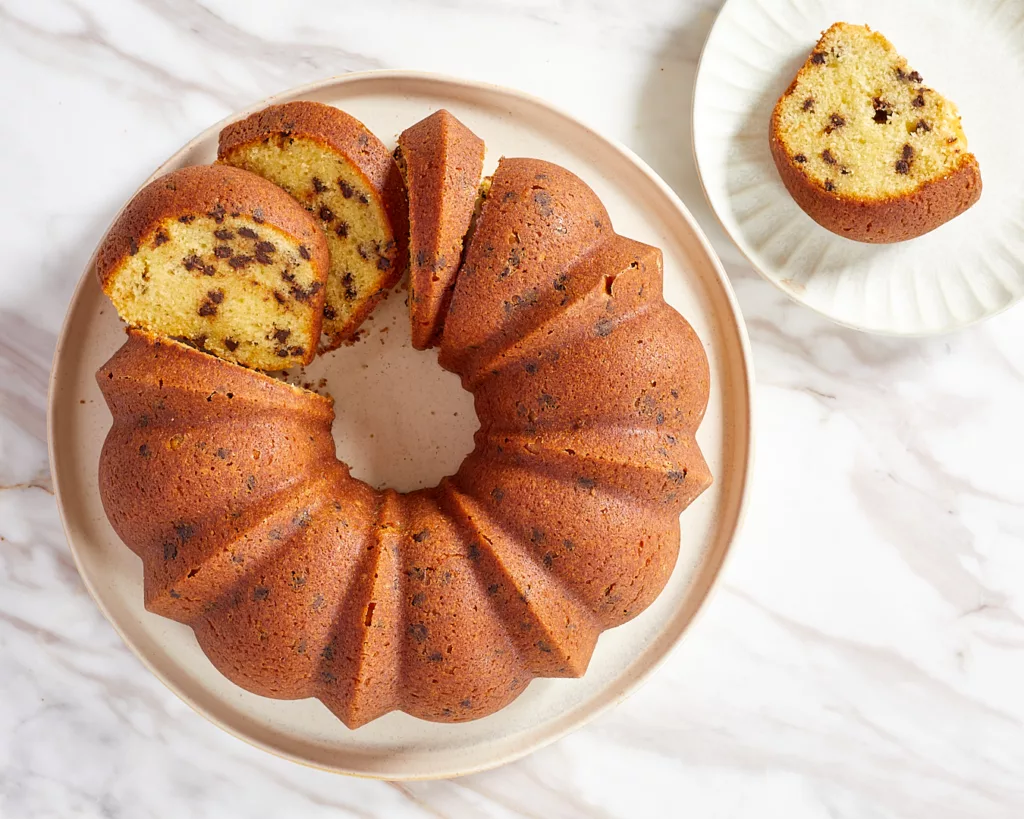 a sour cream chocolate chip bundt cake on a serving plate cut into slices with a slice on a dessert plate to the side