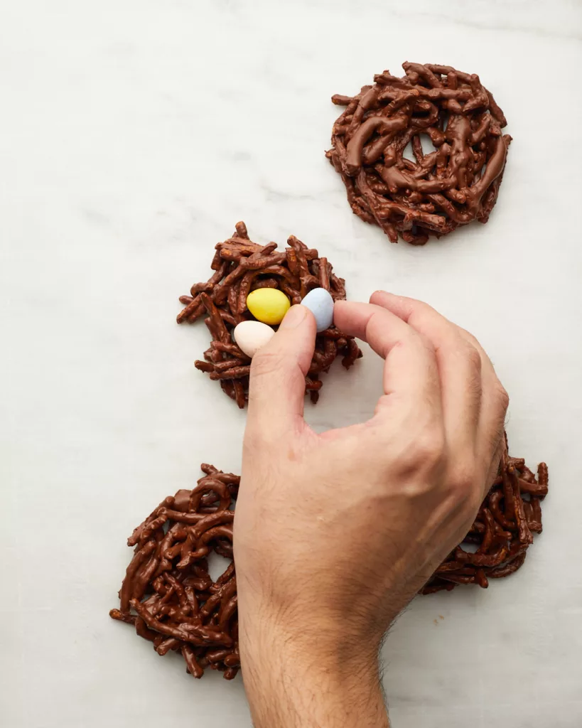 a hand places chocolate candy eggs into birds nest cookies