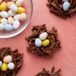 chocolate no-bake easter birds nest cookies with chocolate eggs on a pink background