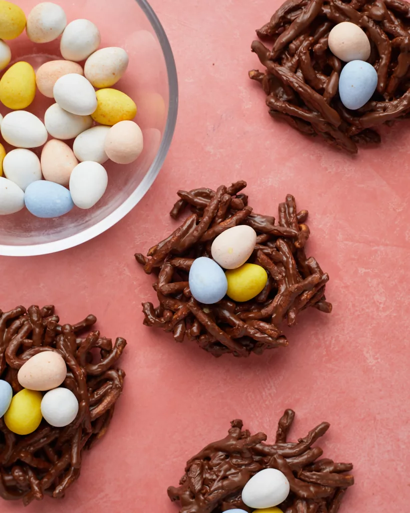 chocolate no-bake easter birds nest cookies with chocolate eggs on a pink background