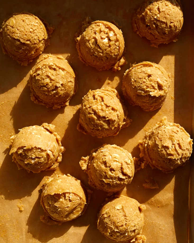 scoops of oatmeal cookie dough sit on a sheet tray lined with parchment paper