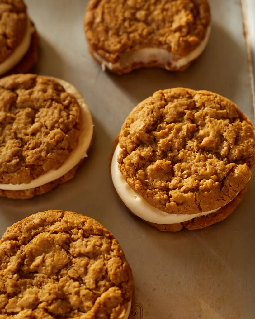 oatmeal sandwich cookies with cream cheese filling sit on a half sheet tray 