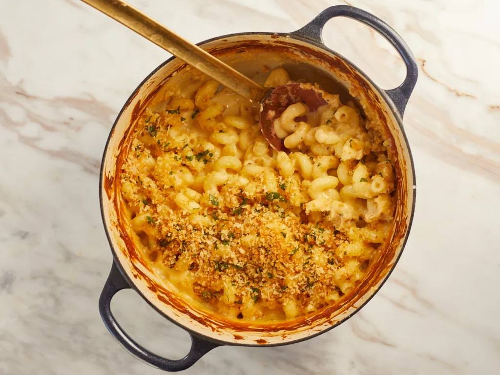 a serving spoon scoops up creamy mac and cheese from a dutch oven pot