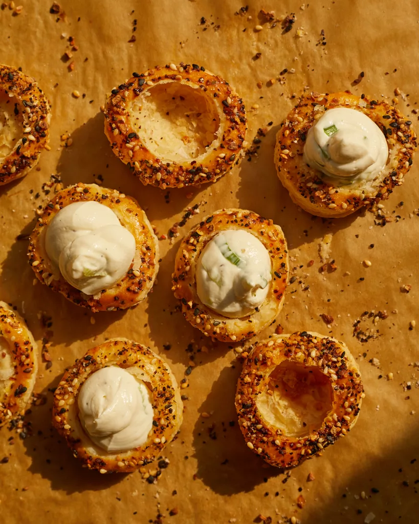 Shells of puff pastry sitting, some empty and some filled with scallion cream cheese