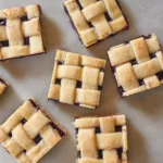 blueberry pie bars with lattice top sliced into squares on a marble background