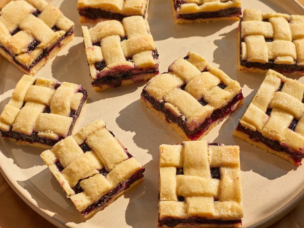 blueberry pie bars with lattice top sliced into squares on a ceramic plate