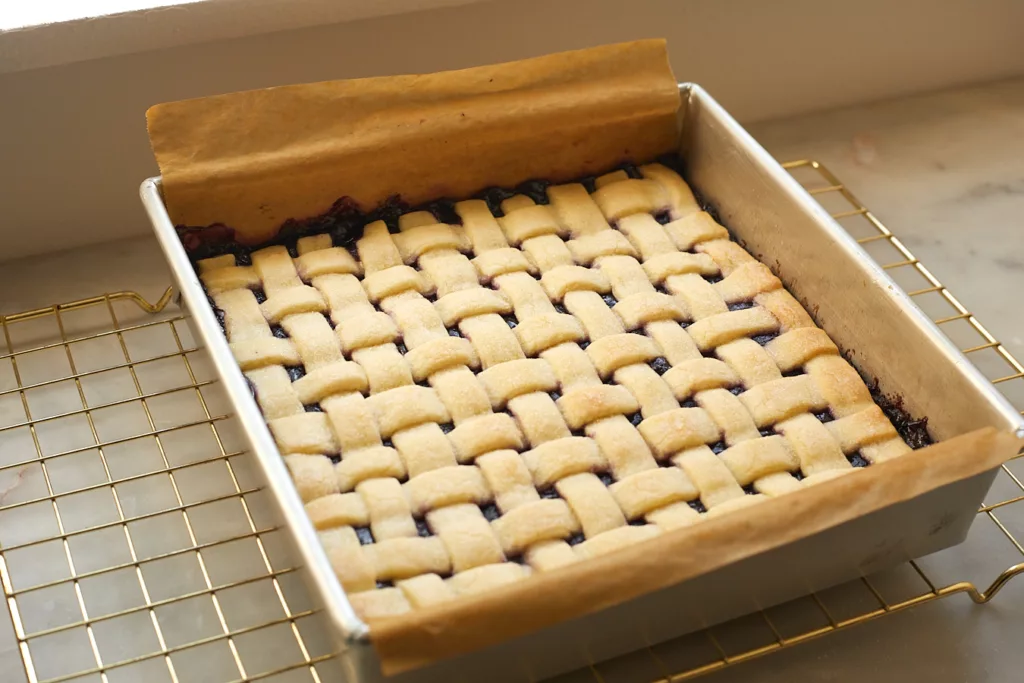 A pan of blueberry pie bars with a lattice crust sitting on a cooling rack