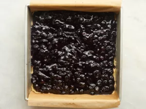 blueberry filling spread onto a cookie crust base in a parchment lined tin