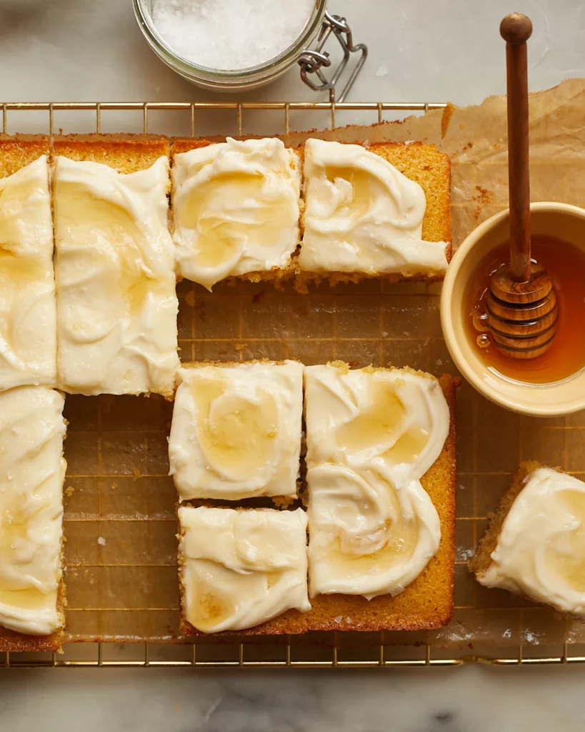 cornbread snacking cake cut into slices on a wire rack surrounded by a pot of honey and a jar of flakey salt