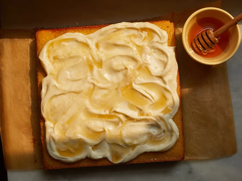 cornbread snacking cake with honey cream cheese frosting on cooling rack next to a pot of honey