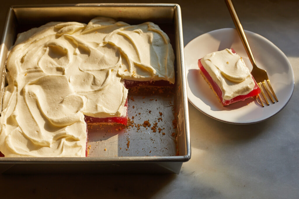 a tin of watermelon strawberry jello bars sits next to a bar sitting on a dessert plate