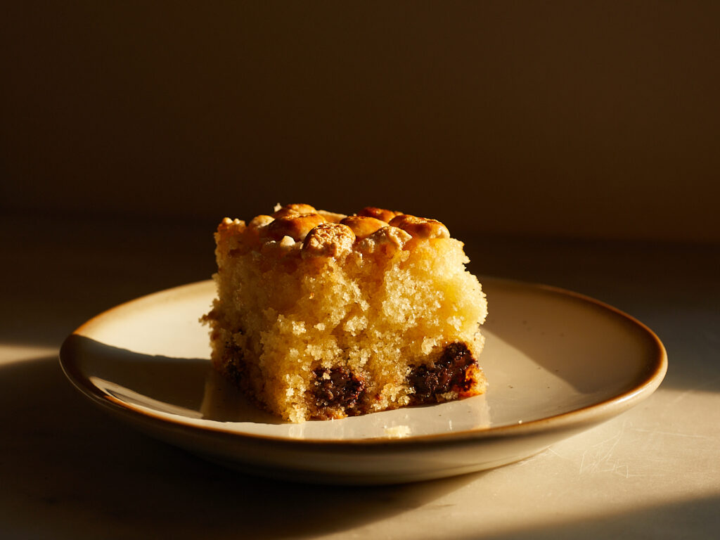 A slice of picnic cake with chocolate chips and marshmallows sits on a dessert plate