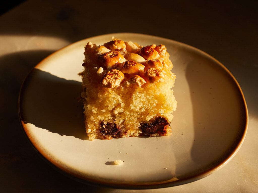 A slice of picnic cake with chocolate chips and marshmallows sits on a dessert plate 