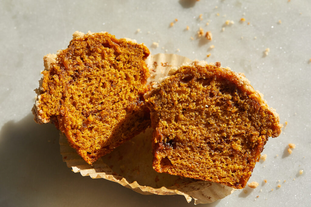 A pumpkin muffin is cut in half, showing the interior swirls of espresso cinnamon brown sugar filling