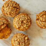 pumpkin muffins with streusel topping sit on a white marble counter