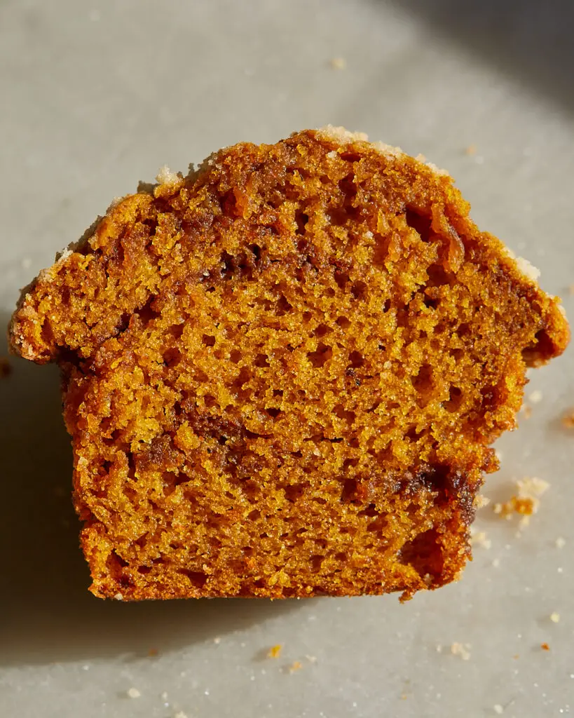 A pumpkin muffin is cut in half, showing the interior swirls of espresso cinnamon brown sugar filling