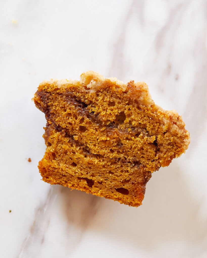 A pumpkin muffin is cut in half, showing the interior swirls of espresso cinnamon brown sugar filling