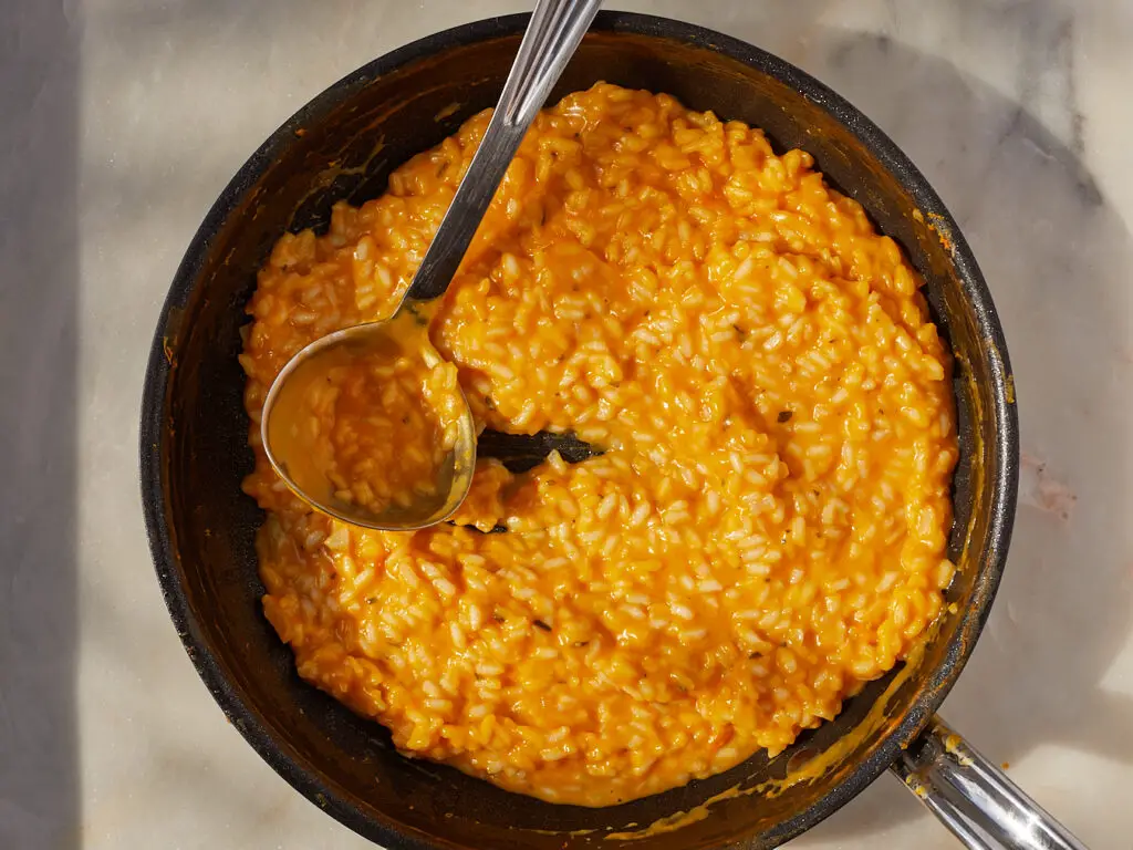 a skillet of cheesy butternut squash risotto with a ladle scooping out of it
