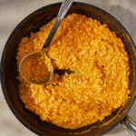 a skillet of cheesy butternut squash risotto with a ladle scooping out of it