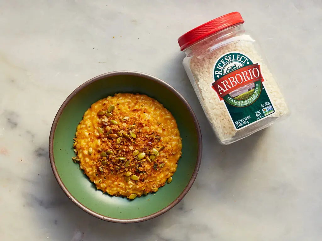 cheesy butternut squash risotto in a green bowl next to a jar of arborio rice