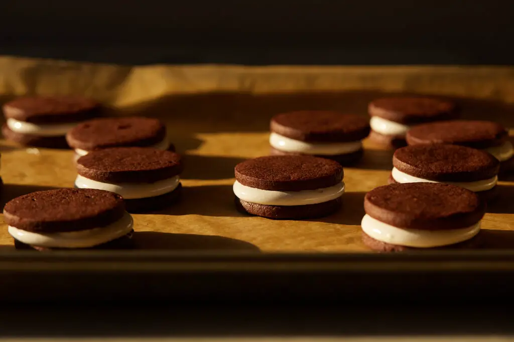 several chocolate cookie sandwiches with peppermint marshmallow filling sit on a parchment lined tray