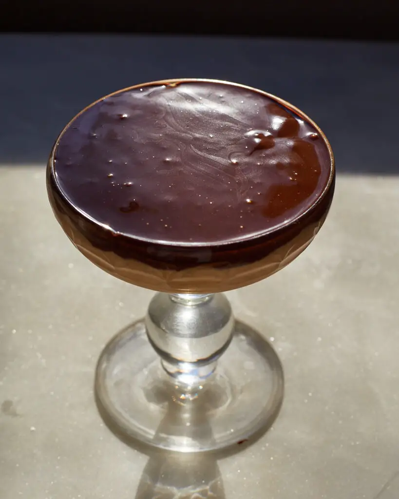 caramel rice pudding with chocolate ganache topping in a crystal glass on a marble surface