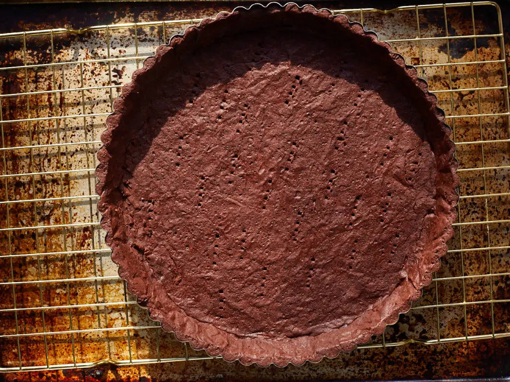 an empty chocolate tart shell sits on a cooling rack