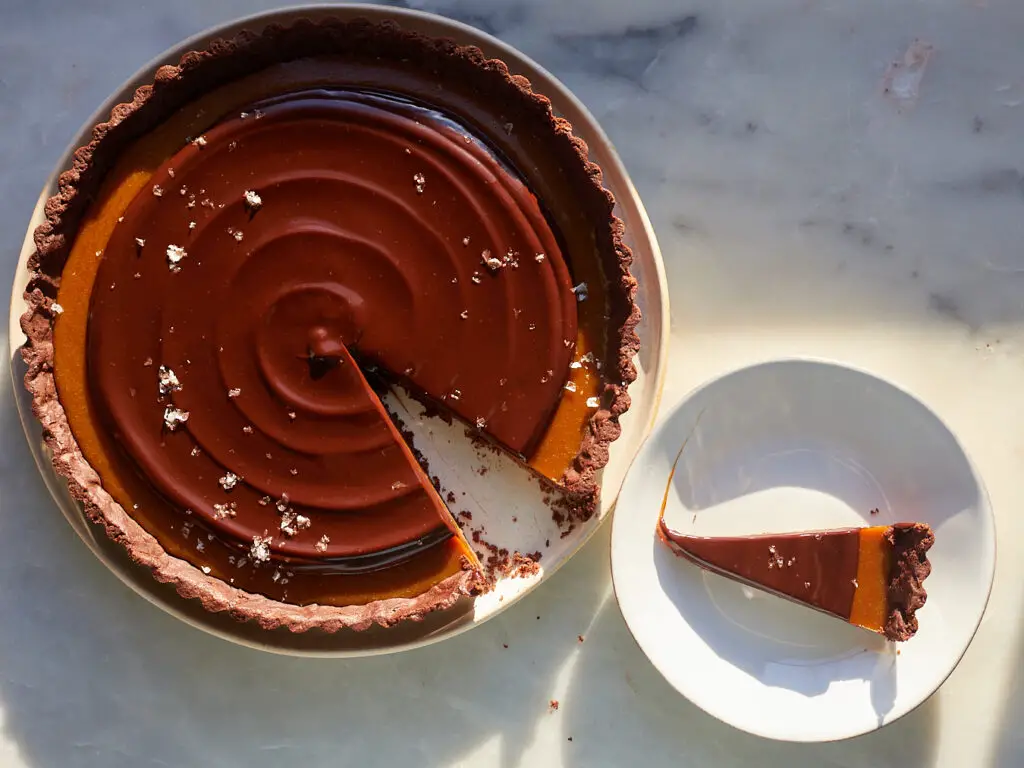 a slice of coffee caramel chocolate tart sits on a dessert plate next to the whole tart