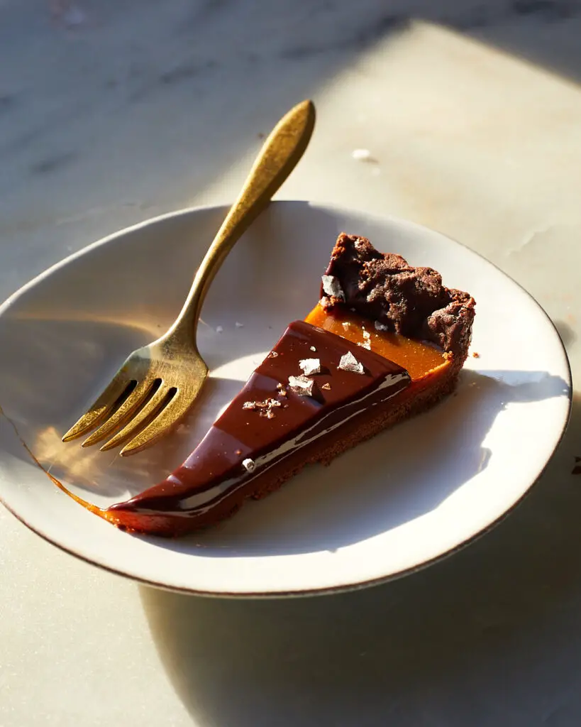 a slice of coffee caramel chocolate tart with a sprinkle of flakey sea salt sits on a dessert plate next to a brass fork