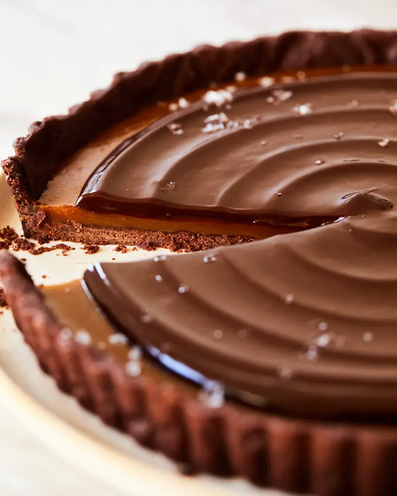 A side view of the cross section of a coffee caramel chocolate tart showing the chocolate ganache, salted caramel and cookie base