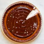 A slice is take out of a coffee caramel chocolate tart on a white serving plate