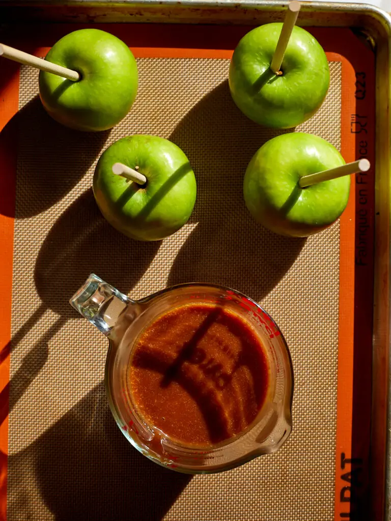 green granny smith apples sitting on a baking sheet next to a measuring cup of caramelv