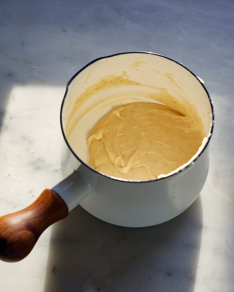 a small pot on a marble surface contains cooked brown butter cream filling