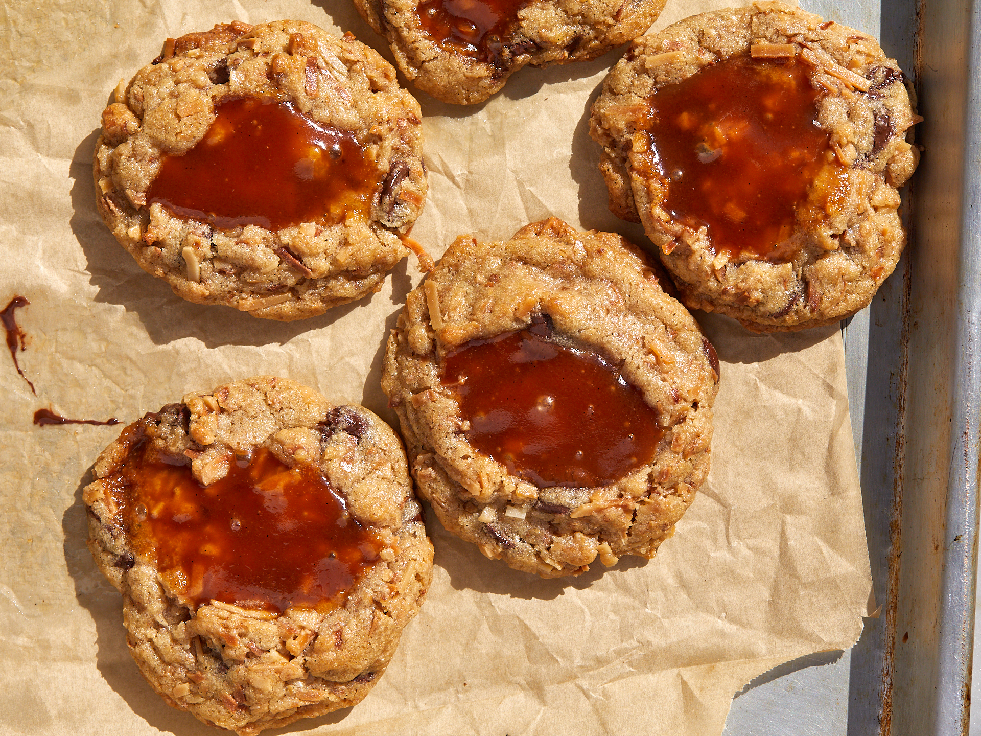 coconut caramel chocolate chip cookies with pools of caramel spilling out on a baking sheet
