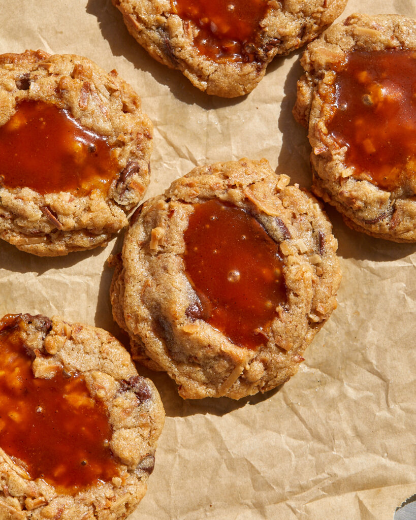 coconut caramel chocolate chip cookies with pools of caramel spilling out on a baking sheet