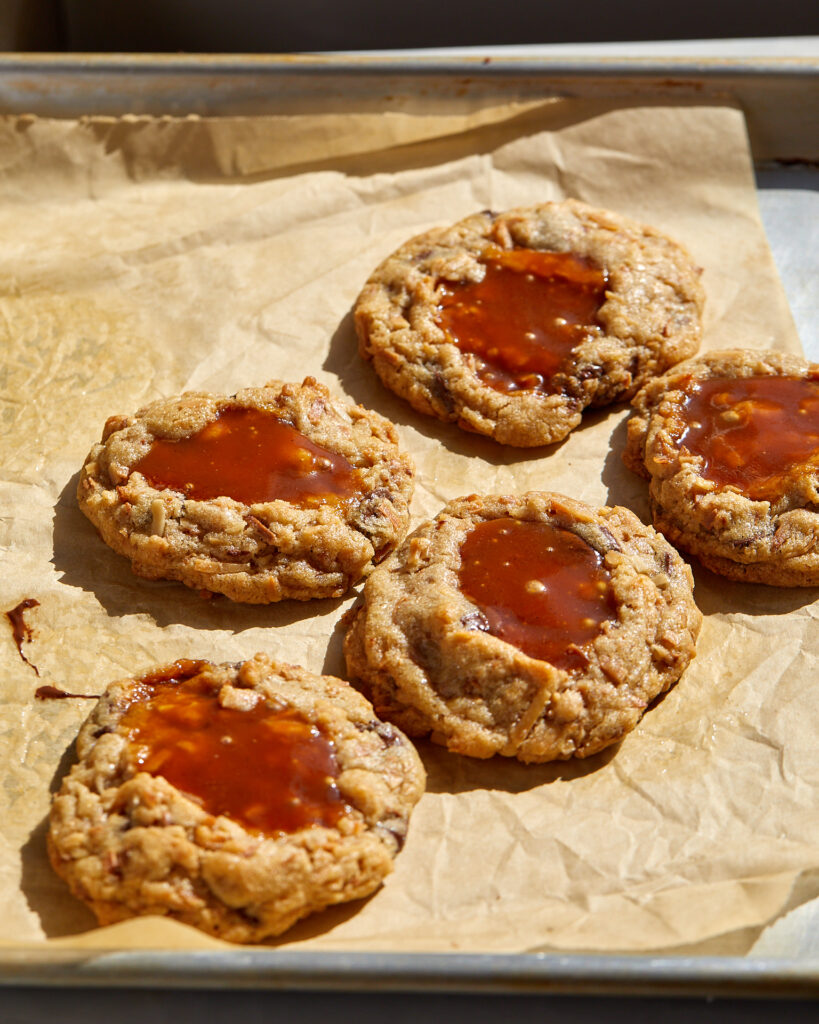 coconut caramel chocolate chip cookies with pools of caramel spilling out on a baking sheet
