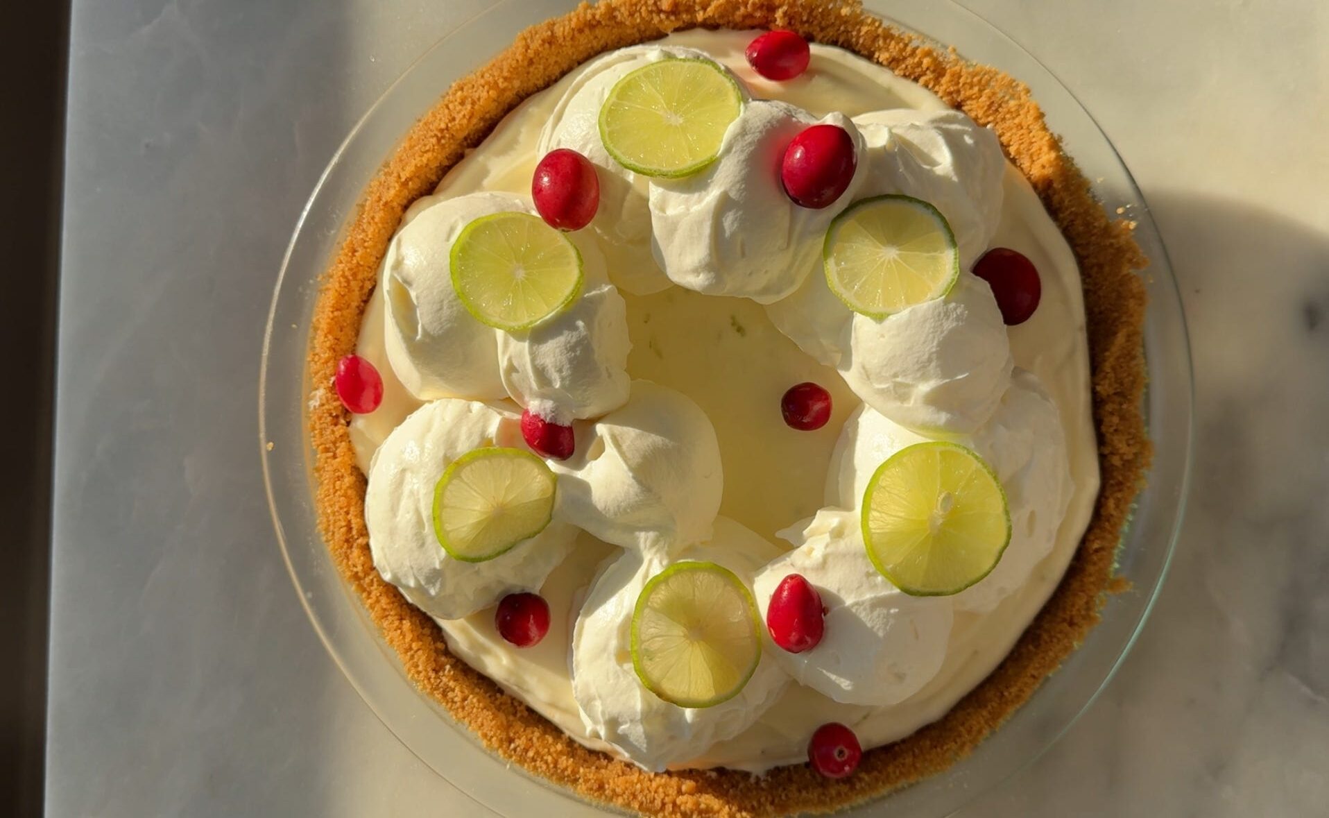 An overhead shot of No-Bake Key Lime Cheesecake pie with whipped cream topping, key lime slices and cranberries
