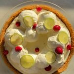An overhead shot of No-Bake Key Lime Cheesecake pie with whipped cream topping, key lime slices and cranberries