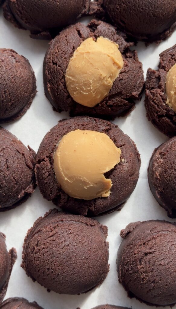 Balls of peanut butter filling being pressed into chocolate cookie dough for buckeye cookies