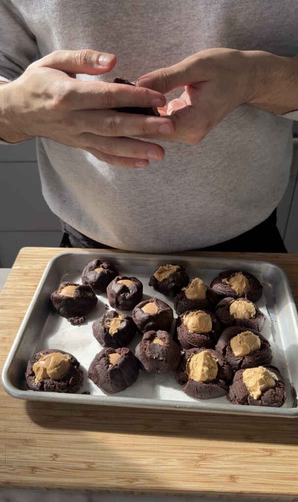 Balls of peanut butter filling being pressed into chocolate cookie dough for buckeye cookies