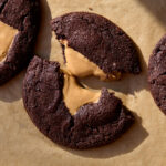A broken chocolate cookie with gooey peanut butter filling on a parchment lined baking sheet