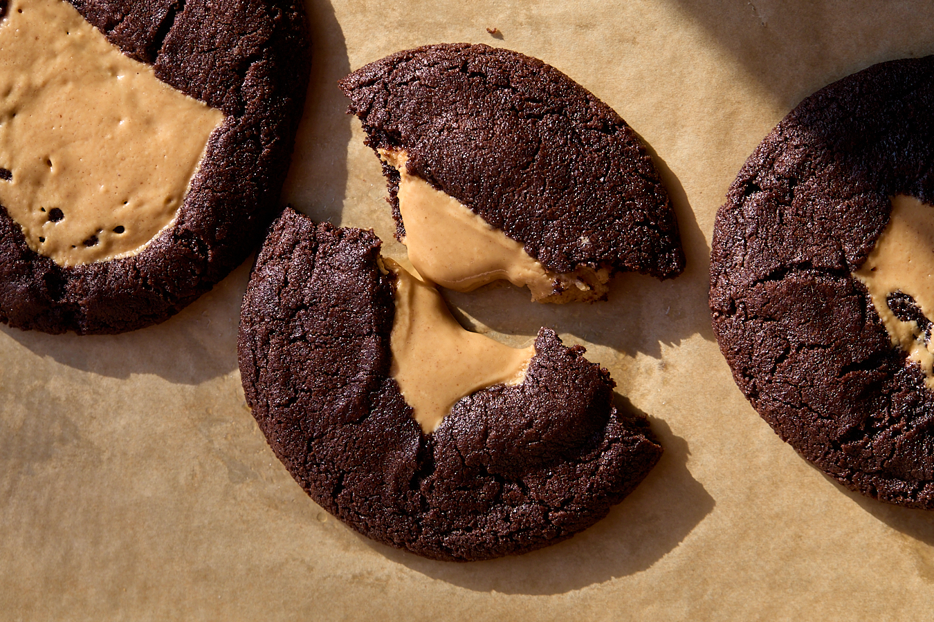 A broken chocolate cookie with gooey peanut butter filling on a parchment lined baking sheet